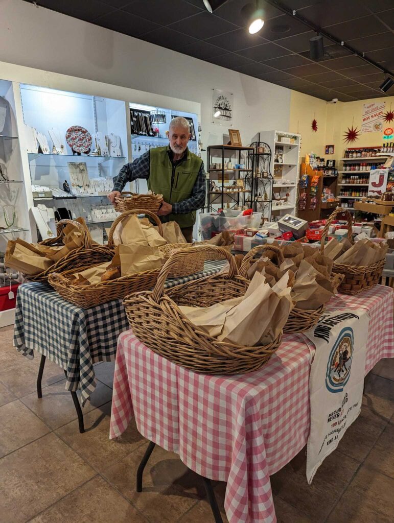 Man setting up wicker baskets filled with goods on tables covered in checkered cloths in a shop.