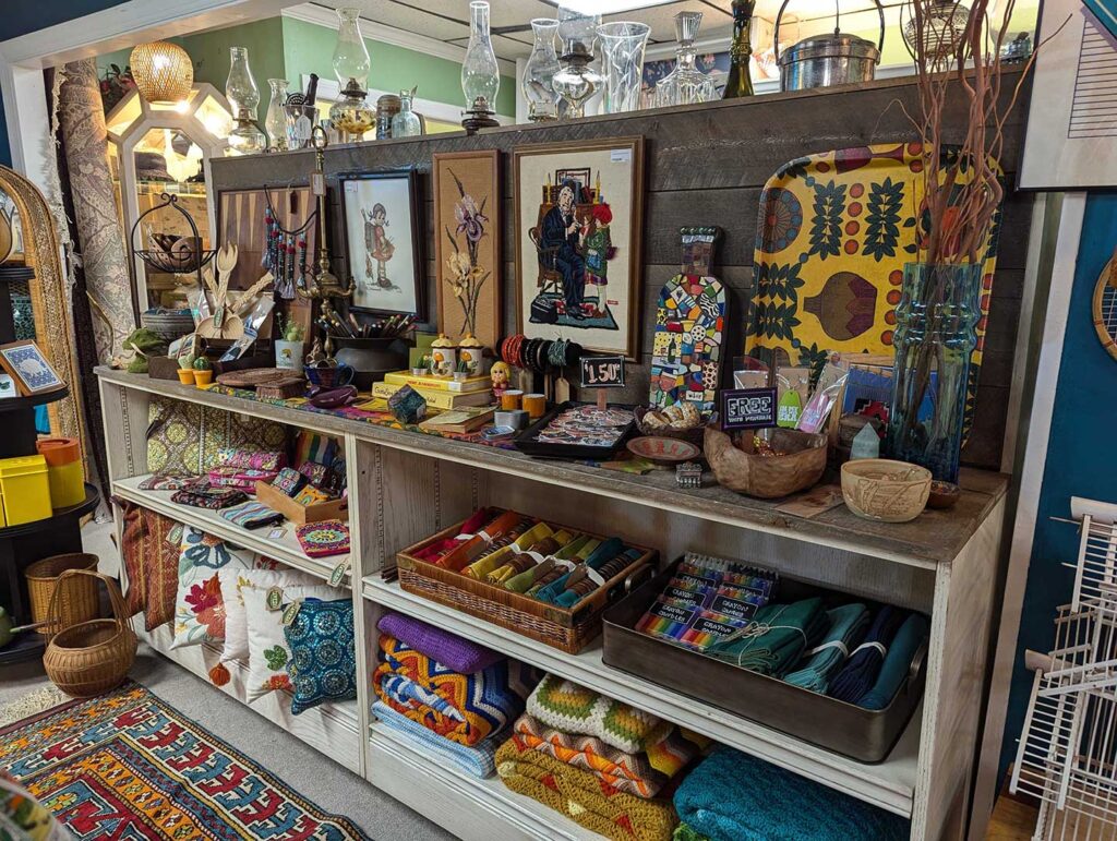 Colorful display of handmade crafts, textiles, and decor items on shelves in a rustic shop.