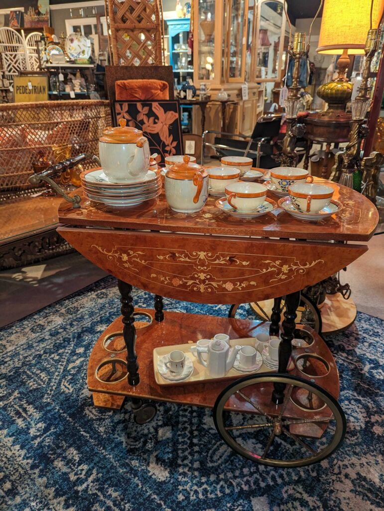 Ornate vintage tea cart with tea set, displayed in an antique shop with eclectic decor.