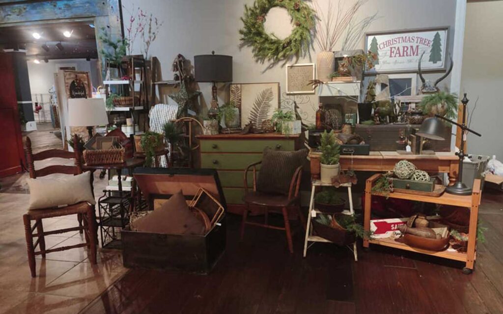 Rustic decor display with greenery, vintage furniture, holiday signs, and various farmhouse-style accents.