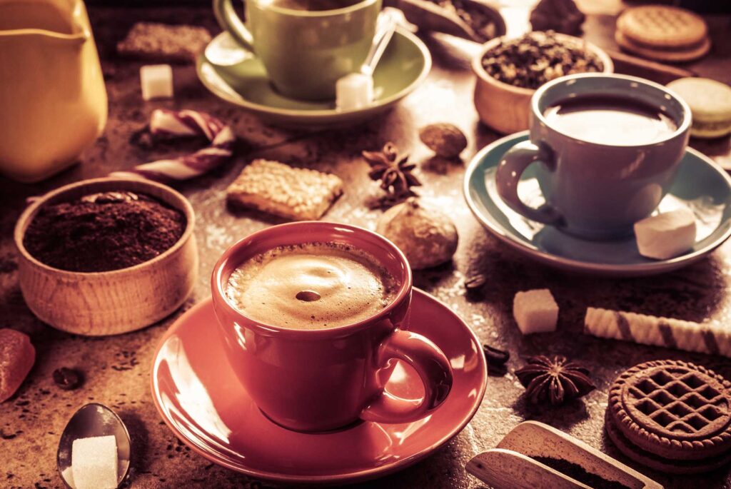 Assorted coffee cups with sugar cubes, cookies, and spices on a rustic table setting.