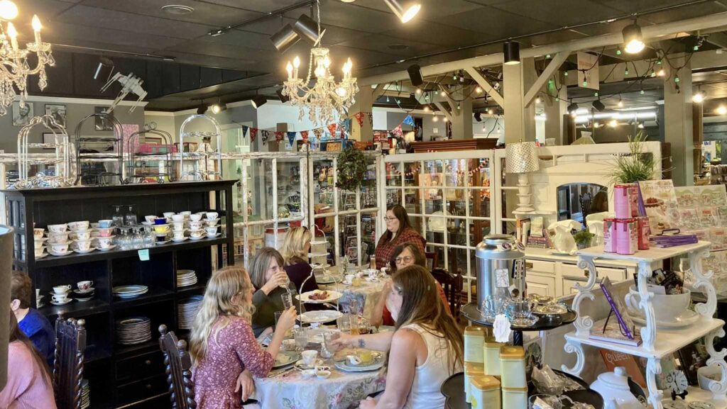 Customers enjoying tea in a cozy, vintage-themed cafe with chandeliers, teacups, and decorative displays.